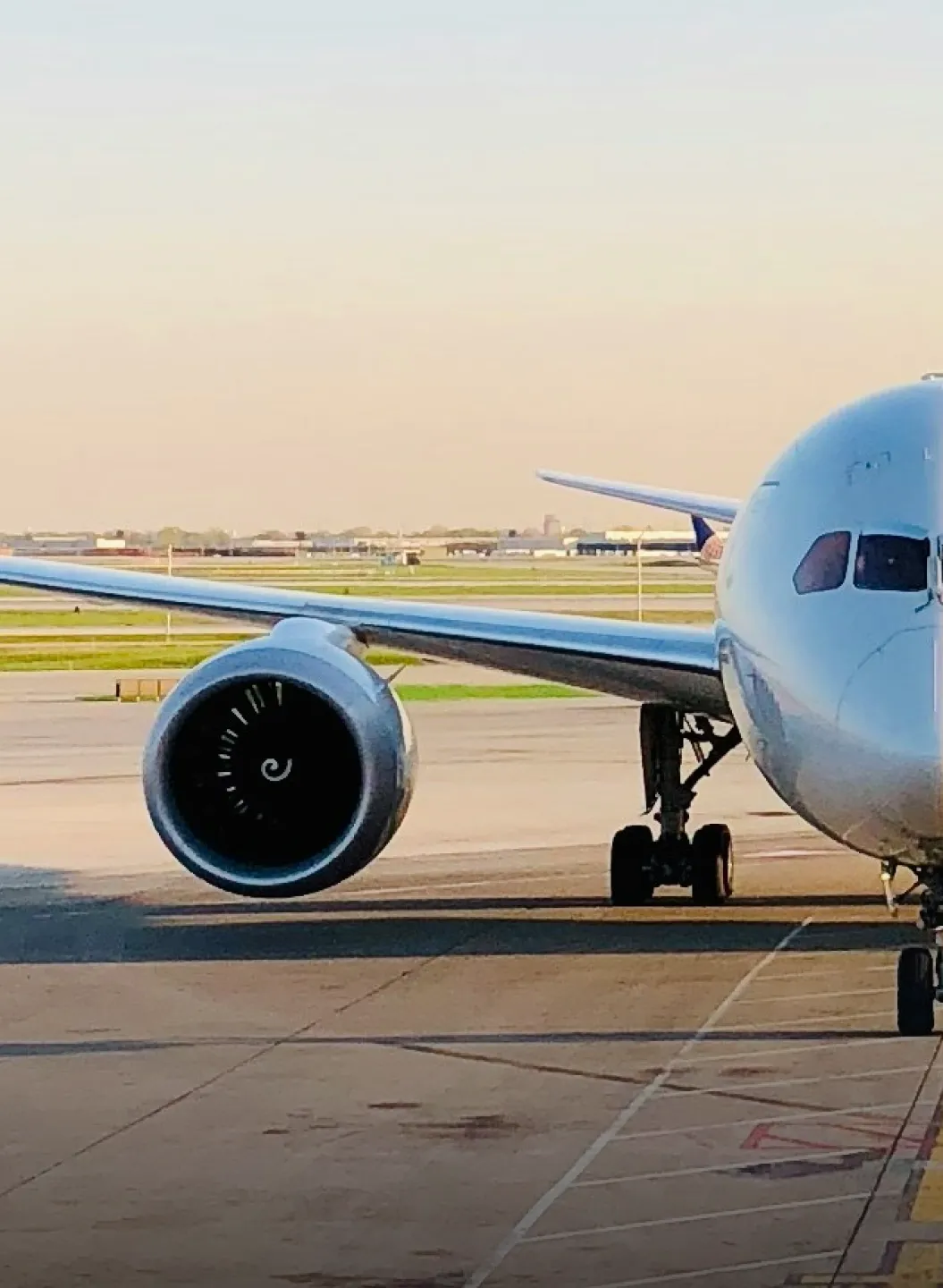 Front left side of a large white airplane parked on a runway at an airport.